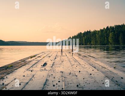 Una lunga banchina di legno si estende in un tranquillo lago che riflette le sfumature dorate del tramonto. Foto Stock