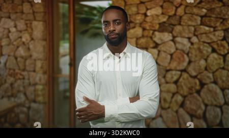 Uomo in camicia bianca con le braccia incrociate e le mani visibili all'ingresso dell'edificio in pietra, guardando verso l'alto; contemplazione premurosa. Foto Stock