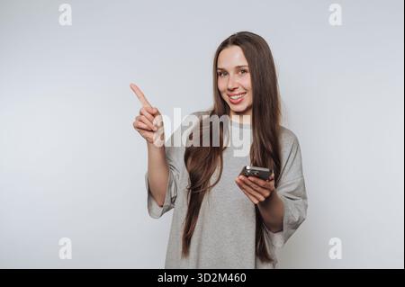 Donna sorridente che tiene lo smartphone e punta verso l'alto Foto Stock