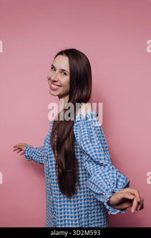 Donna sorridente in abito a scacchi blu su sfondo rosa. Foto Stock