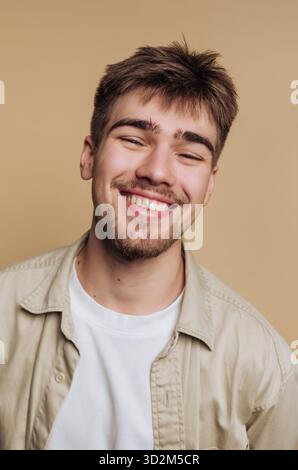Giovane sorridente con la barba sullo sfondo beige. Foto Stock
