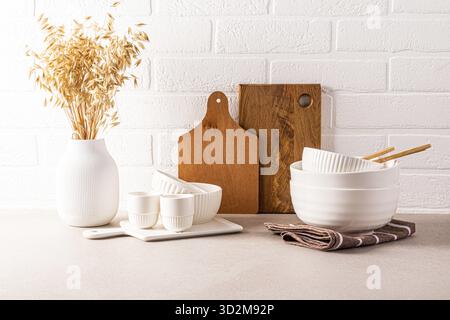 Splendido sfondo della cucina moderno piano di lavoro con un set di utensili da cucina, ciotole ed elementi decorativi. Vista frontale. Muro bianco di mattoni Foto Stock