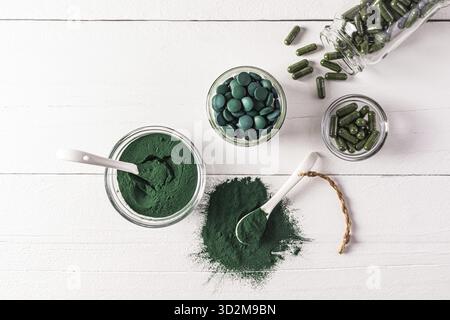 Tavolette di alghe spirulina naturali rotonde blu-verdi e polvere in ciotola su sfondo bianco. vaso medico con capsule di alghe. Integratori alimentari naturali Foto Stock