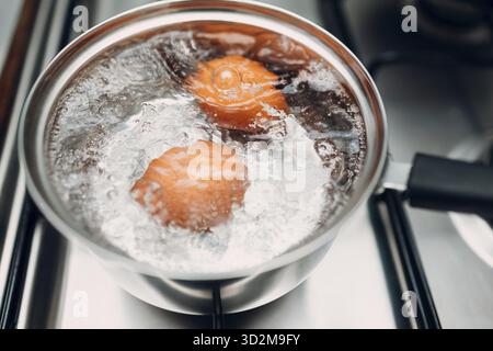 Pentola in acciaio inossidabile con uova bollenti, colazione in acqua su un piano cottura a gas Foto Stock