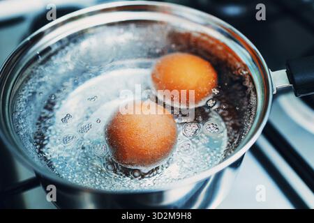 Pentola in acciaio inossidabile con uova bollite per colazione in acqua bollente con vista dall'alto della stufa a gas Foto Stock
