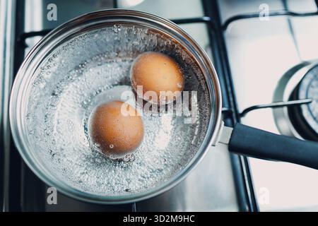 Pentola in acciaio inossidabile con due uova bollenti, colazione in acqua con vista dall'alto su una stufa a gas Foto Stock