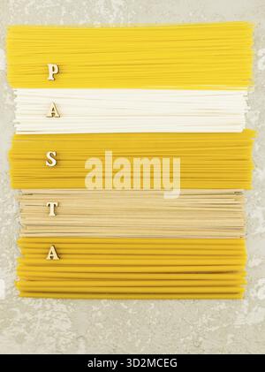 Vista dall'alto piatta verticale di varie paste secche italiane su sfondo grigio. lettere di legno con la parola - pasta Foto Stock