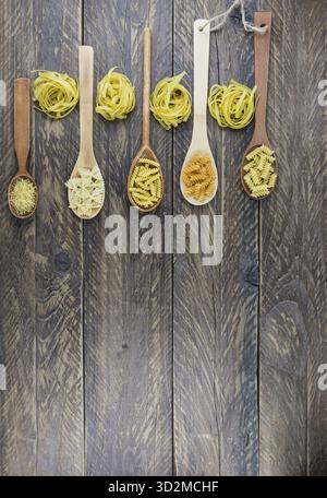 Vista verticale piana di cucchiai di legno di vario genere e forma di pasta secca. Tavole rustiche di legno Foto Stock