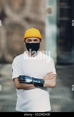 Giovane disabile con mano protesica artificiale che indossa una maschera medica protettiva Foto Stock