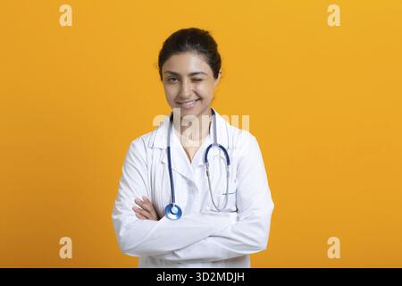 Ritratto di indiano wink medico donna in bianco abito medico stetoscopio isolato su sfondo giallo Foto Stock
