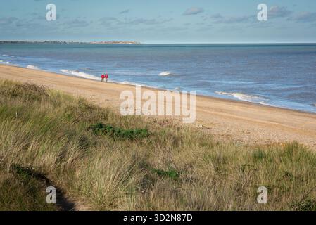 Una coppia di anziani che cammina da sola su una spiaggia deserta di Suffolk, Inghilterra, Regno Unito, e si affaccia sulle dune di sabbia di una coppia di anziani Foto Stock