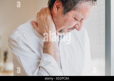 Uomo d'affari non rasato che soffre di grave dolore al collo, che tiene il collo in disagio in ufficio, uomo stressato che sente tensione e rigidità. Focu selettiva Foto Stock