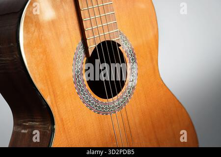 Buco sonoro e corde di una chitarra acustica in legno rossastro, parte di uno strumento musicale, sfondo grigio, messa a fuoco selezionata, profondità di fiel stretta Foto Stock