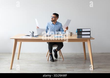 Responsabile arabo specializzato che esamina i documenti finanziari mentre lavora presso la sua Office Desk Foto Stock