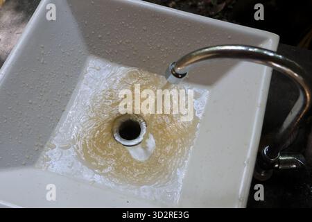 L'acqua fluente riempie il lavandino quadrato bianco, creando increspature e motivi vorticosi mentre drena. il rubinetto metallico risplende sopra, con gocce d'acqua Foto Stock