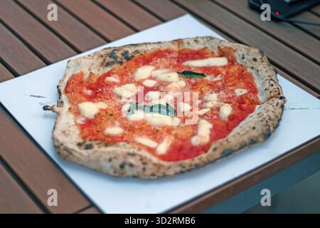 Primo piano di una tradizionale pizza margherita napoletana condita con salsa di pomodoro, mozzarella fusa e basilico fresco servito su un vassoio di carta Foto Stock