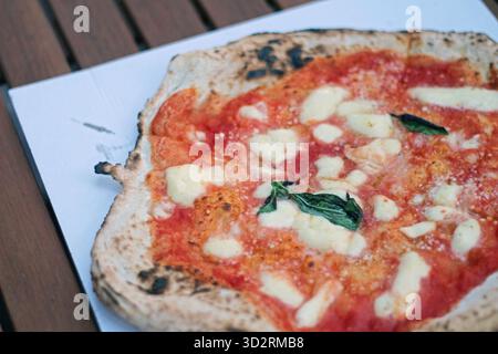 Primo piano di una tradizionale pizza margherita napoletana condita con salsa di pomodoro, mozzarella fusa e basilico fresco servito su un vassoio di carta Foto Stock