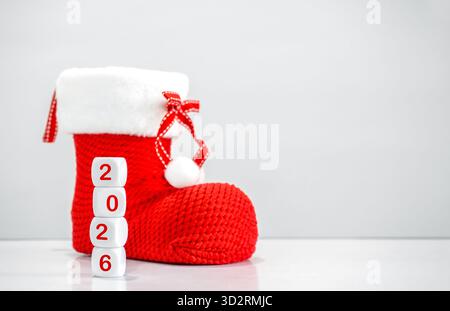 Composizione minima di calze natalizie rosse e blocchi di dadi che mostrano 2026 su sfondo bianco. Perfetto per festività di Capodanno e Natale Foto Stock