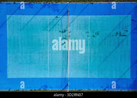 Vista dall'alto del campo da tennis esterno con superficie usurata. Vista aerea del campo sportivo blu con linee visibili e rete. Concetto di ricreazione, attività all'aperto e infrastrutture sportive Foto Stock