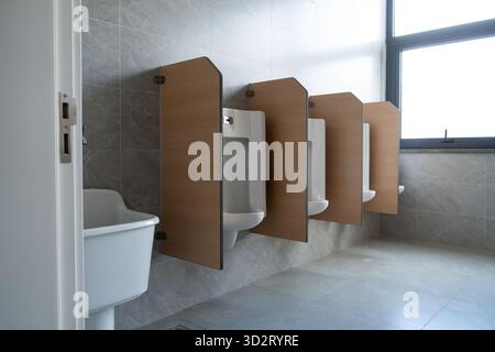 orinatoio bianco con pareti divisorie in legno, con piastrelle grigie in un bagno da uomo pulito Foto Stock