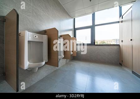 orinatoio bianco con pareti divisorie in legno, con piastrelle grigie in un bagno da uomo pulito Foto Stock