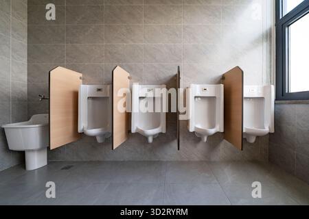 orinatoio bianco con pareti divisorie in legno, con piastrelle grigie in un bagno da uomo pulito Foto Stock