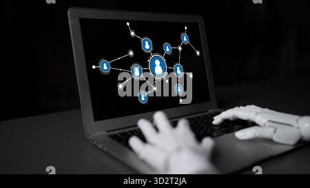 Una mano robotica interagisce con un laptop visualizzando una rete di icone di profilo, simboleggiando la fusione di tecnologia e comunicazione in un'era digitale. Foto Stock