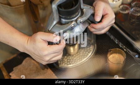 Barista concentrato che prepara caffè fresco con il macinacaffè manuale. processo di preparazione della bevanda espresso mattutina con attrezzature professionali in un accogliente caffè Foto Stock