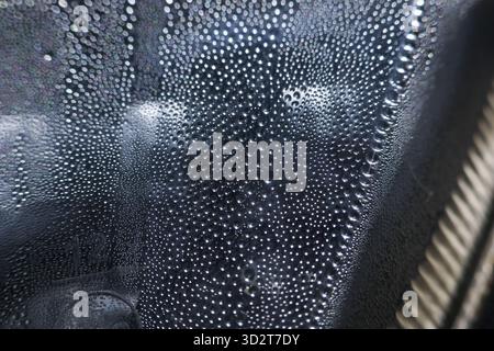 Getto macro calmo di condensa a goccia d'acqua. la rugiada umida si forma su una superficie di sfondo astratta scura. rinfrescante sensazione di umidità e liquido puro sul vetro Foto Stock