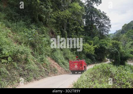 Camion rosso in viaggio guidando su strade sterrate attraverso la giungla tropicale. il modo rurale in montagna crea un senso di avventura, viaggio e trasporto in rem Foto Stock