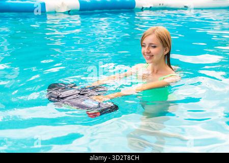 Donna sorridente in piscina che usa uno scooter d'acqua, che ama le attività estive, Foto Stock