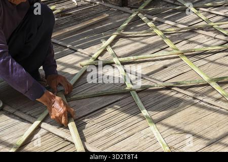 Lavoratore diligente tessendo a mano il pavimento in bambù tradizionale. I dettagli mirati dell'artigianato e della costruzione mostrano un motivo geometrico naturale, mettendo in mostra l'abilità manuale Foto Stock