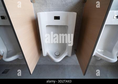 orinatoio bianco con pareti divisorie in legno, con piastrelle grigie in un bagno da uomo pulito Foto Stock