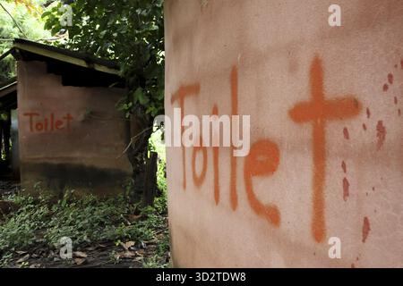 Bagno rustico all'aperto e attico con cartello arancione dipinto a mano sul muro di fango. semplice capanna rurale con servizi igienici di base, scenario desolato che riflette la povert Foto Stock