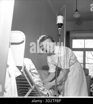 Trasfusione di sangue negli anni '1950 Un'infermiera che indossa un badge Sophiahemmet sull'uniforme con un paziente accanto a un supporto che regge un flacone di sangue etichettato O. il gruppo sanguigno è indicato come o (la lettera o, non zero). È uno degli otto gruppi sanguigni principali del sistema ABO, insieme A A, B e AB, e può essere o RH-positivo (o+) o RH-negativo (o-). La designazione o indica l'assenza di antigeni A o B sulla superficie dei globuli rossi. Kungsholmen, Stoccolma, 18 febbraio 1952 Conard rif. 1931 Foto Stock