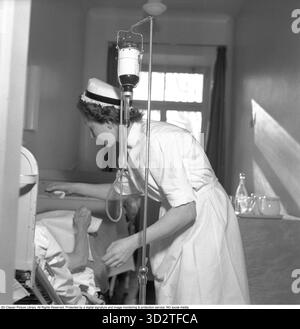 Trasfusione di sangue negli anni '1950 Un'infermiera che indossa un badge Sophiahemmet sull'uniforme con un paziente accanto a un supporto che regge un flacone di sangue etichettato O. il gruppo sanguigno è indicato come o (la lettera o, non zero). È uno degli otto gruppi sanguigni principali del sistema ABO, insieme A A, B e AB, e può essere o RH-positivo (o+) o RH-negativo (o-). La designazione o indica l'assenza di antigeni A o B sulla superficie dei globuli rossi. Kungsholmen, Stoccolma, 18 febbraio 1952 Conard rif. 1931 Foto Stock