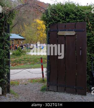 Un cancello in legno rustico collocato in un arco di siepe si apre su un parco pieno di colori autunnali. Foto Stock