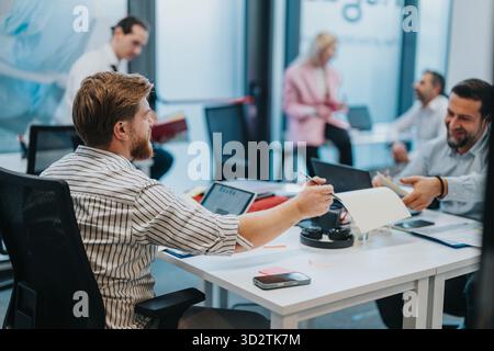 Il team di un ufficio affollato collabora alla stesura di documenti e condivide idee intorno a una scrivania Foto Stock
