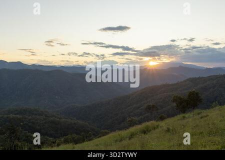 Tranquillo paesaggio montano al tramonto con splendida e tranquilla vista sulla verde valle. il sole che tramonta dietro il cielo nuvoloso crea un momento panoramico e tranquillo Foto Stock