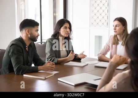 Il team di lavoro ascolta il collega alla scrivania per conferenze in un ufficio moderno Foto Stock