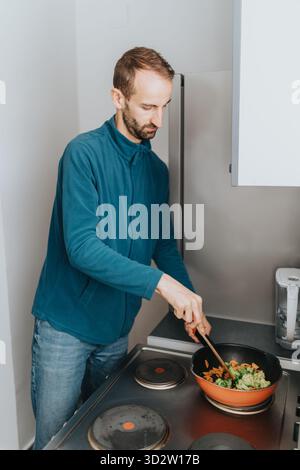 Uomo che cucina le verdure in una pentola su un piano cottura moderno Foto Stock
