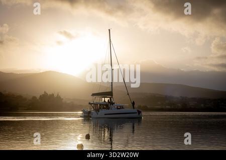 Uno yacht da vacanza che naviga attraverso un canale di mare con il sole del mattino che sorge sulle colline lontane. Foto Stock