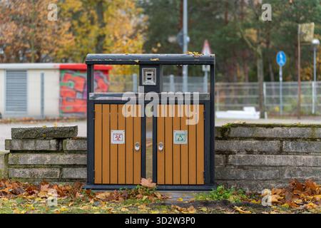 Moderno cestino esterno a due scomparti per il riciclaggio e i rifiuti. Circondato da foglie autunnali cadute e blocchi di pietra. Foto Stock