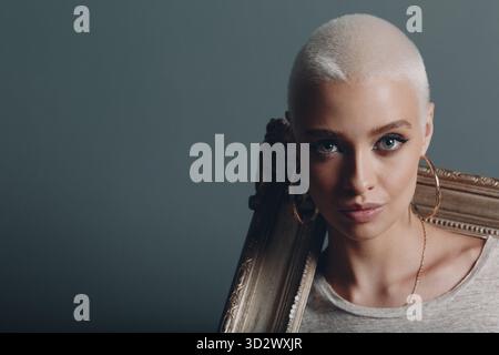 Millenial giovane donna dai capelli corti e biondi color argento tiene la cornice dorata delle mani sul ritratto del collo delle spalle Foto Stock