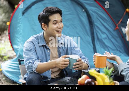Una coppia felice che condivide caffè e risate in un campeggio, circondato dalla natura. Un momento perfetto di connessione e avventura all'aria aperta Foto Stock