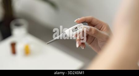 Una persona tiene in mano un termometro digitale per controllare la temperatura corporea, evidenziando la consapevolezza della salute e l'auto-monitoraggio Foto Stock