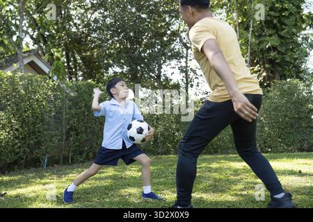 Un momento di gioia in cui padre e figlio giocano a calcio nel loro cortile, mostrando amore e stile di vita attivo Foto Stock