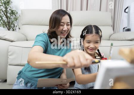 Una madre e una figlia gioiose che si divertono a dipingere insieme, promuovendo la creatività nel loro ambiente domestico Foto Stock