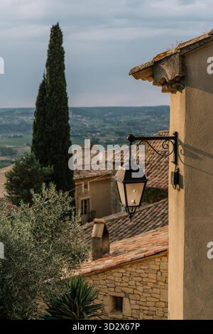 Antico villaggio in pietra con tetti in terracotta, una lanterna vintage su un muro, un cipresso e una luce soffusa che si affaccia sulla campagna. Foto Stock