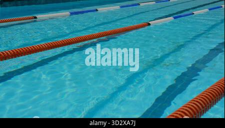 L'acqua scintillante della piscina riflette la luce del sole nella piscina all'aperto, con divisori di corsia rosso bianco e blu Foto Stock